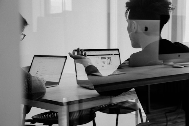 Two IDM Technologies team members collaborating on laptops in a modern office